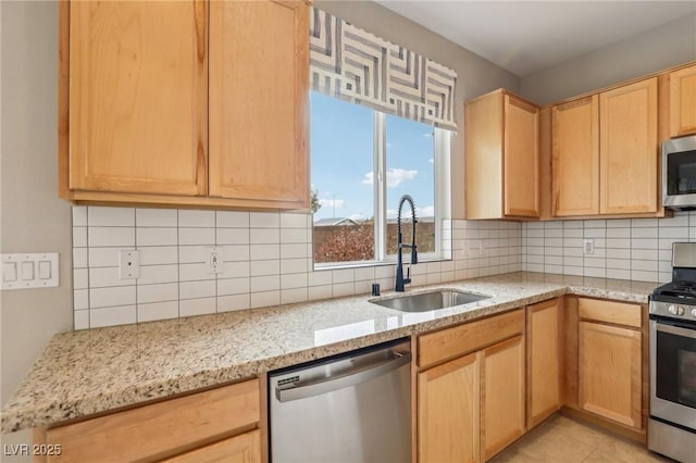 kitchen with light stone counters, light brown cabinets, a sink, stainless steel appliances, and backsplash