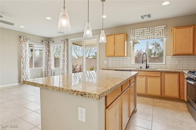 kitchen featuring visible vents, light brown cabinets, a sink, backsplash, and gas range