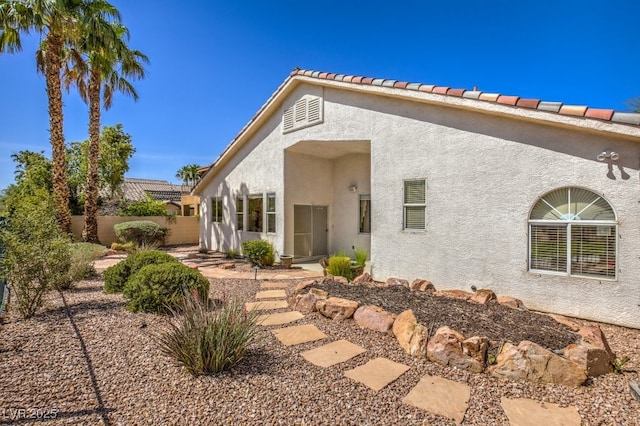 rear view of house with stucco siding and fence