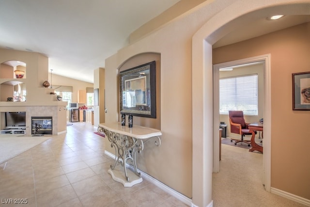 corridor with vaulted ceiling, light tile patterned floors, baseboards, and light carpet