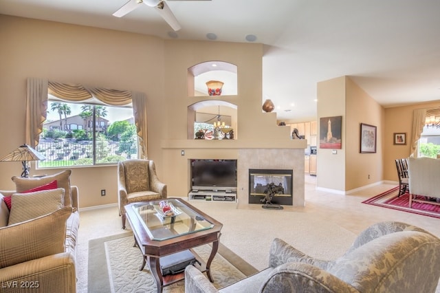 carpeted living area with ceiling fan with notable chandelier, baseboards, and a tile fireplace