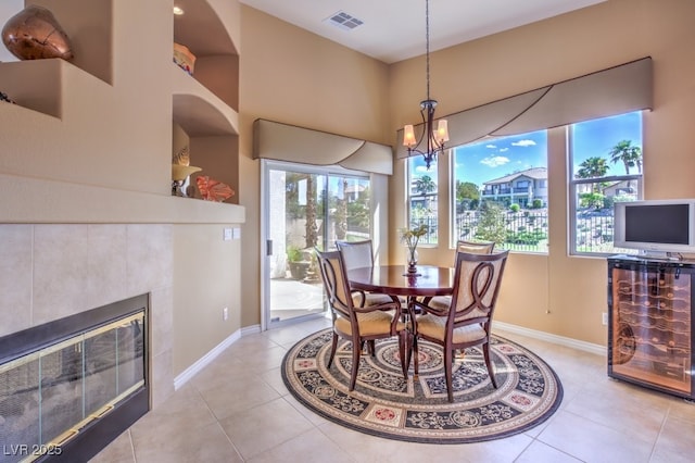 dining area with visible vents, baseboards, a tiled fireplace, light tile patterned flooring, and a notable chandelier