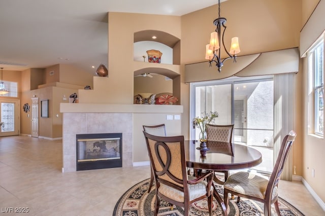 dining area featuring baseboards, light tile patterned floors, a fireplace, a high ceiling, and an inviting chandelier