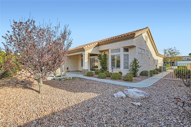 view of side of home featuring stucco siding, a tile roof, a patio, and fence