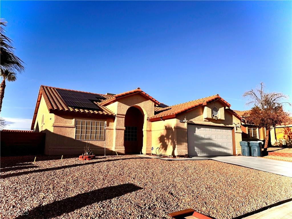 mediterranean / spanish-style home featuring a tile roof, roof mounted solar panels, stucco siding, a garage, and driveway