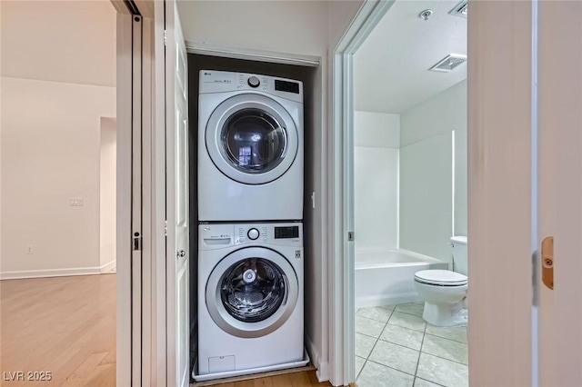 clothes washing area featuring visible vents, stacked washer and dryer, laundry area, and tile patterned flooring