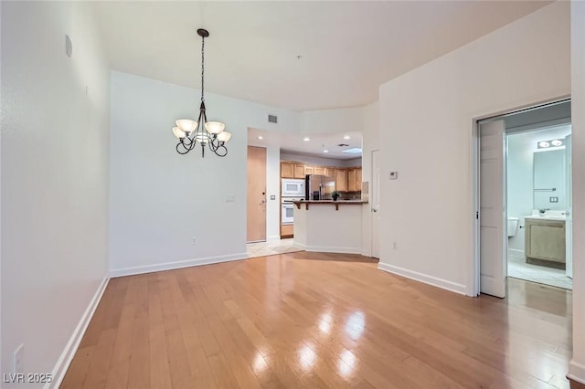 unfurnished dining area featuring visible vents, baseboards, light wood-type flooring, and an inviting chandelier