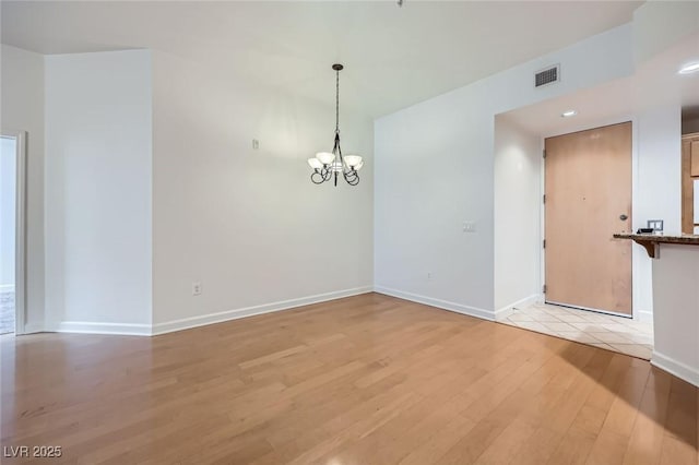 empty room featuring an inviting chandelier, light wood-style floors, visible vents, and baseboards