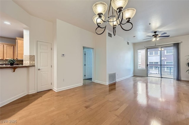 unfurnished dining area with light wood-type flooring, visible vents, baseboards, and ceiling fan with notable chandelier