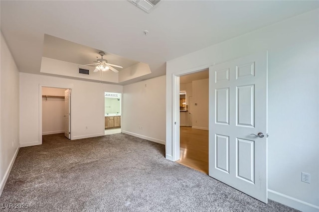 unfurnished bedroom featuring baseboards, visible vents, carpet floors, a spacious closet, and a raised ceiling