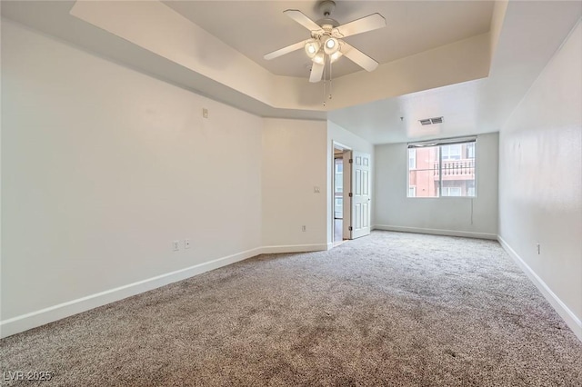 spare room with visible vents, carpet, baseboards, a tray ceiling, and a ceiling fan