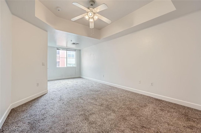 empty room with visible vents, baseboards, a tray ceiling, ceiling fan, and carpet flooring