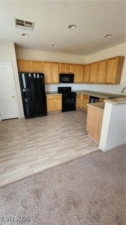 kitchen with visible vents, light colored carpet, black appliances, and light wood-style floors