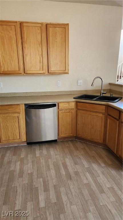 kitchen with light wood finished floors, light countertops, brown cabinets, stainless steel dishwasher, and a sink