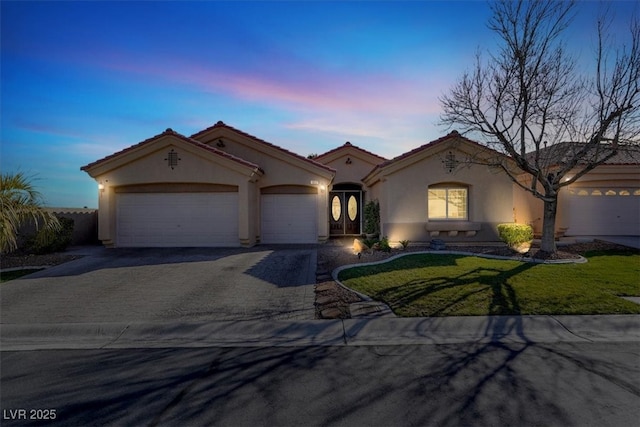 mediterranean / spanish house with driveway, an attached garage, stucco siding, a tiled roof, and a lawn