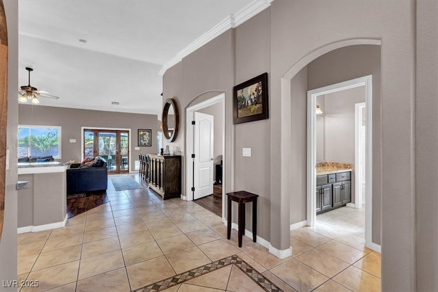 hallway featuring light tile patterned floors, arched walkways, baseboards, and ornamental molding