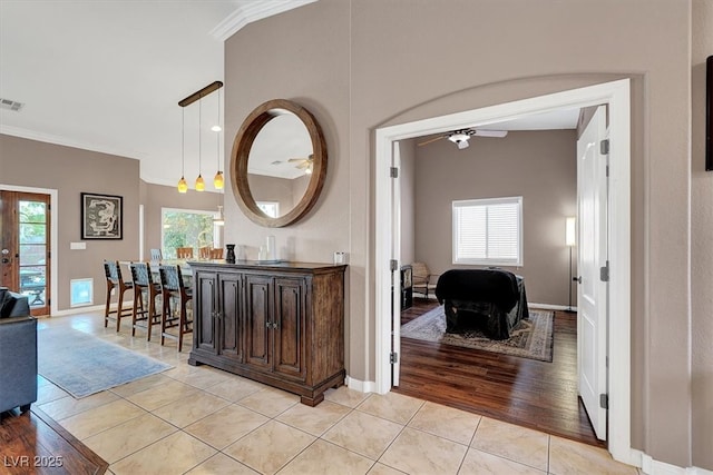 corridor featuring light tile patterned flooring, visible vents, baseboards, and ornamental molding