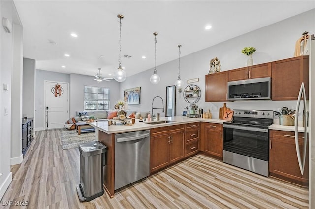 kitchen with light countertops, appliances with stainless steel finishes, a peninsula, a ceiling fan, and a sink