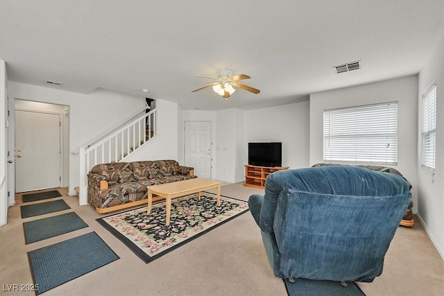 living room with visible vents, light colored carpet, stairway, and a ceiling fan