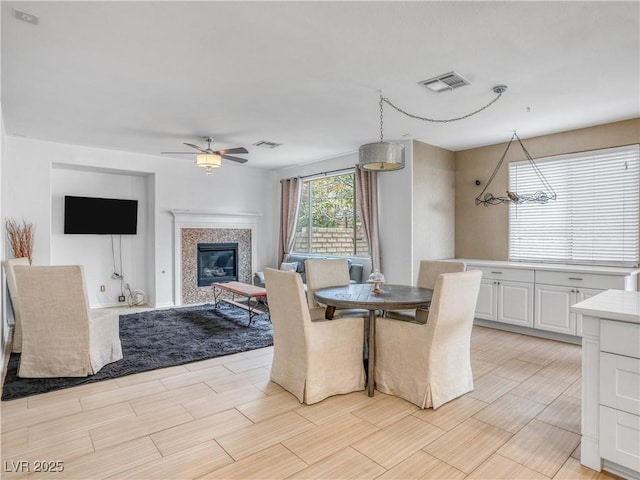 dining space with a glass covered fireplace, visible vents, and ceiling fan