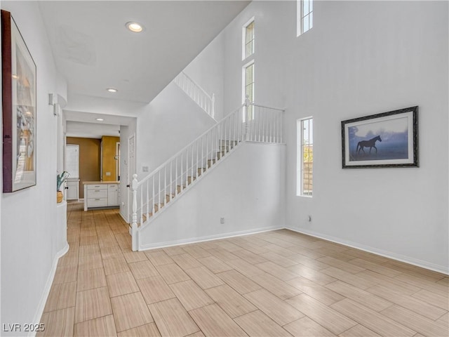 foyer entrance with baseboards, wood tiled floor, stairway, recessed lighting, and a towering ceiling