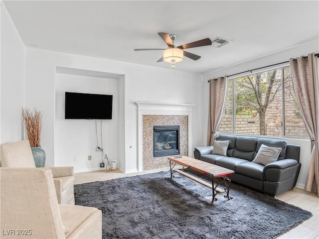 living area featuring visible vents, baseboards, ceiling fan, and a glass covered fireplace