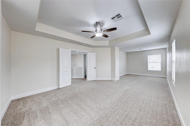 unfurnished room featuring visible vents, light carpet, a raised ceiling, baseboards, and ceiling fan