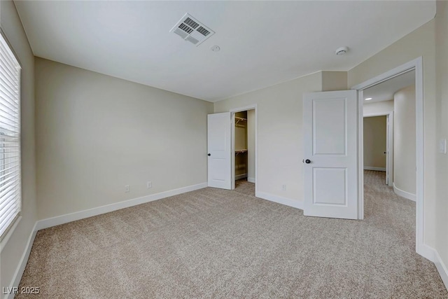 unfurnished bedroom featuring visible vents, light carpet, baseboards, and a spacious closet