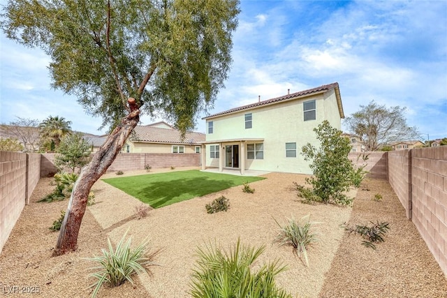 back of house with a fenced backyard, stucco siding, a yard, and a patio