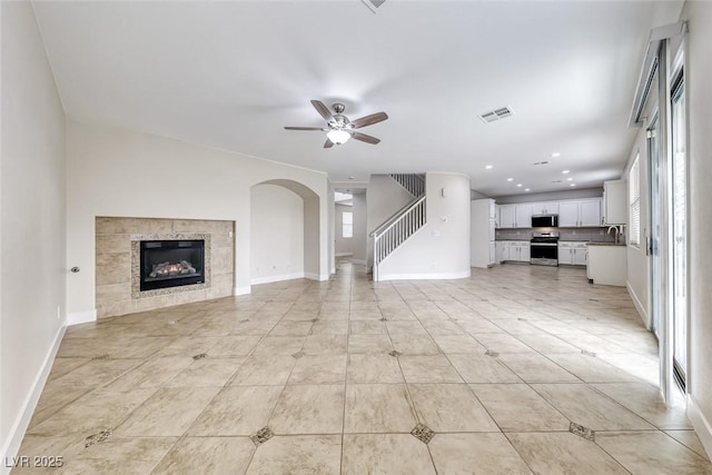 unfurnished living room featuring visible vents, baseboards, ceiling fan, a tile fireplace, and a sink