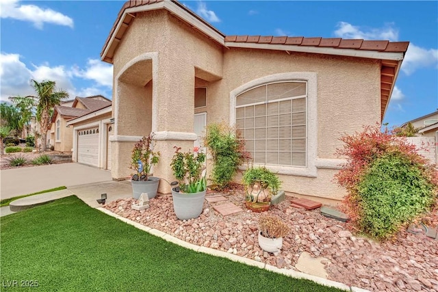 view of front facade with stucco siding, driveway, a tile roof, and a garage