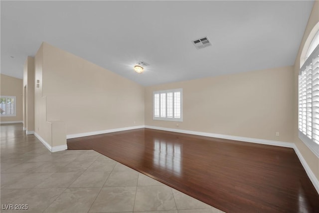 tiled spare room featuring visible vents, plenty of natural light, baseboards, and lofted ceiling