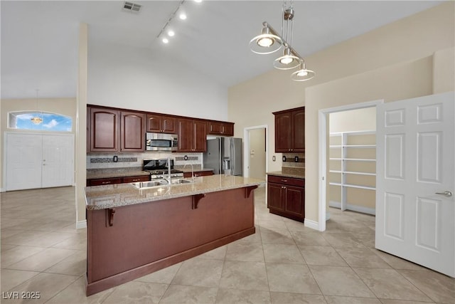 kitchen with light stone countertops, a kitchen bar, light tile patterned floors, stainless steel appliances, and high vaulted ceiling