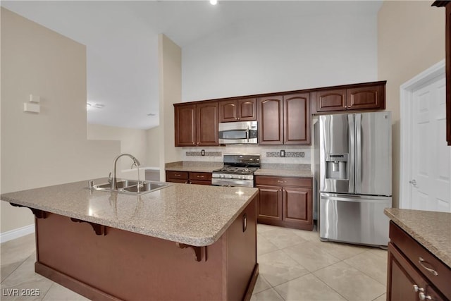 kitchen featuring light tile patterned floors, a sink, a towering ceiling, appliances with stainless steel finishes, and a kitchen breakfast bar