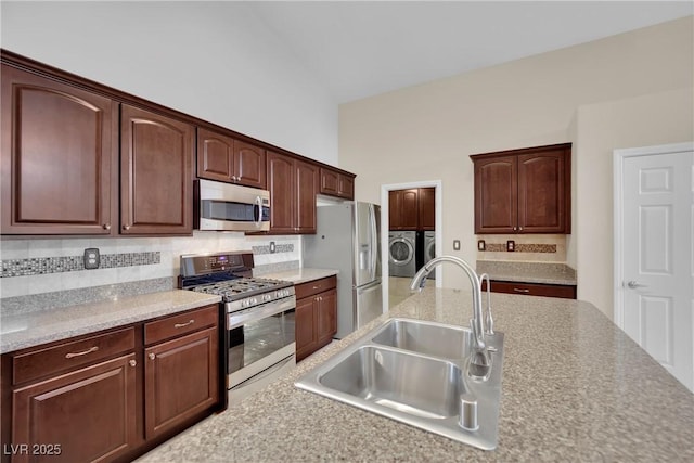 kitchen with washing machine and clothes dryer, backsplash, light countertops, appliances with stainless steel finishes, and a sink