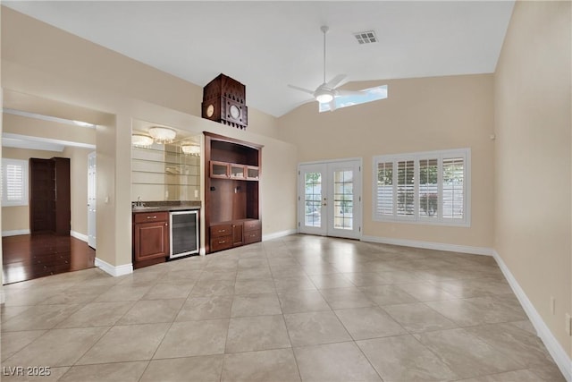 unfurnished living room with visible vents, bar area, ceiling fan, wine cooler, and french doors