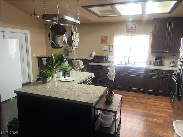 kitchen featuring a sink, a kitchen island, dark brown cabinets, and freestanding refrigerator