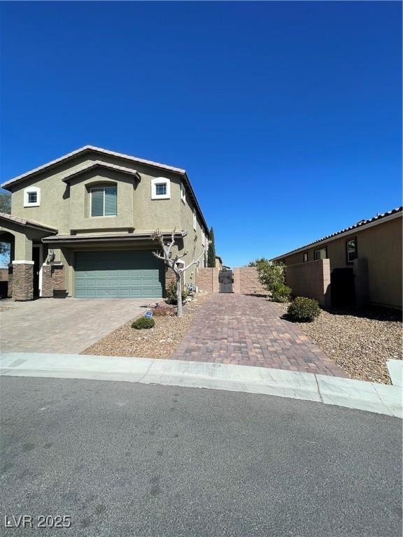 view of front facade with stucco siding, decorative driveway, an attached garage, and fence