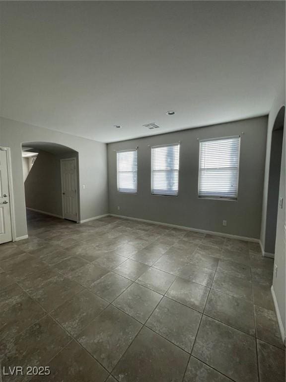 unfurnished room with visible vents, baseboards, and arched walkways