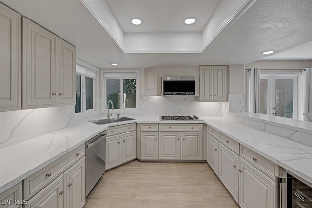 kitchen with a sink, light stone counters, stainless steel appliances, light wood-style floors, and a raised ceiling