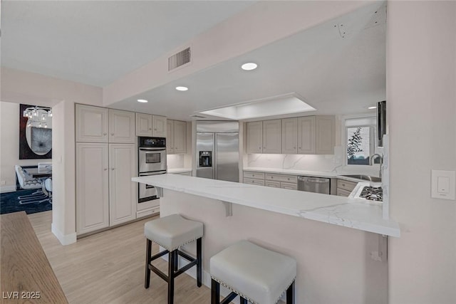 kitchen featuring visible vents, appliances with stainless steel finishes, a peninsula, light wood-style floors, and a sink