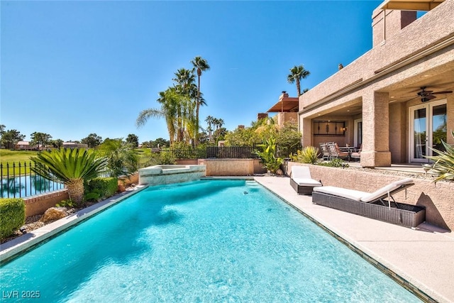 view of pool with a fenced backyard, a pool with connected hot tub, ceiling fan, a water view, and a patio area