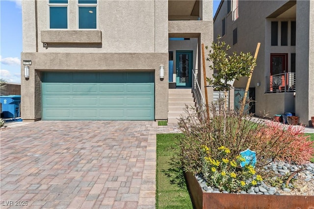 view of front facade with stucco siding, an attached garage, and decorative driveway