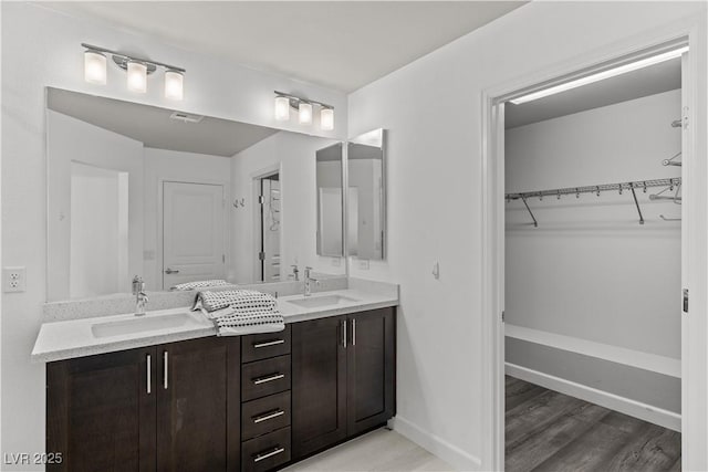 bathroom featuring double vanity, a walk in closet, baseboards, and a sink