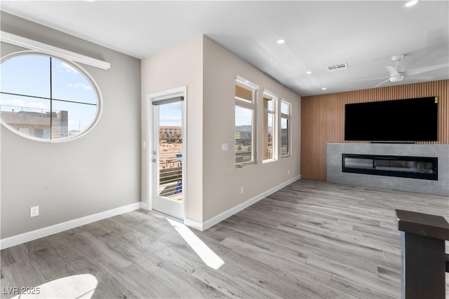 unfurnished living room with a wealth of natural light, visible vents, baseboards, and a ceiling fan