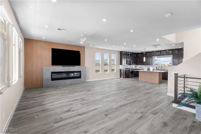 unfurnished living room featuring a ceiling fan, visible vents, light wood finished floors, recessed lighting, and a glass covered fireplace