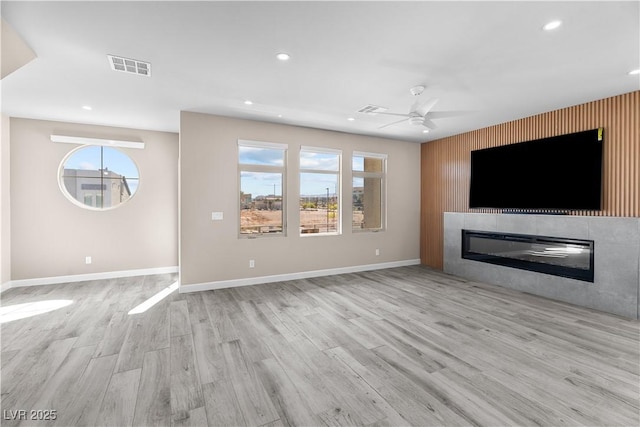 unfurnished living room with visible vents, wood finished floors, baseboards, and a glass covered fireplace