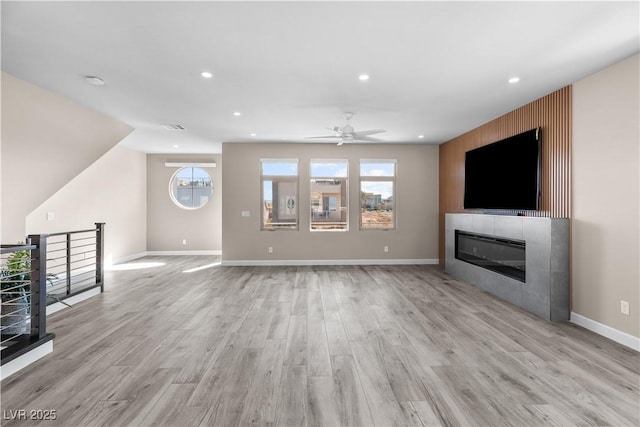 unfurnished living room with visible vents, ceiling fan, a tile fireplace, light wood-type flooring, and a wealth of natural light