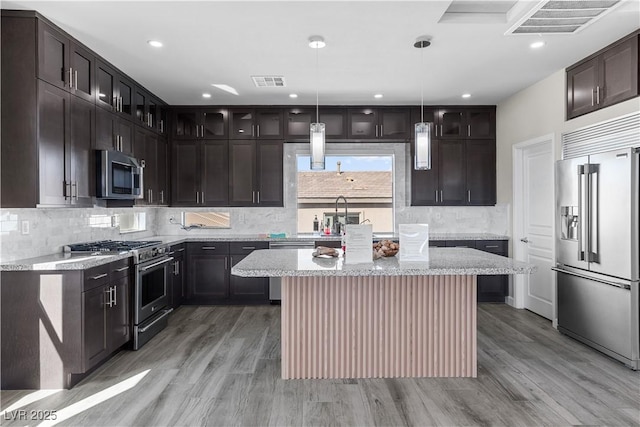 kitchen with light wood-style floors, tasteful backsplash, visible vents, and premium appliances