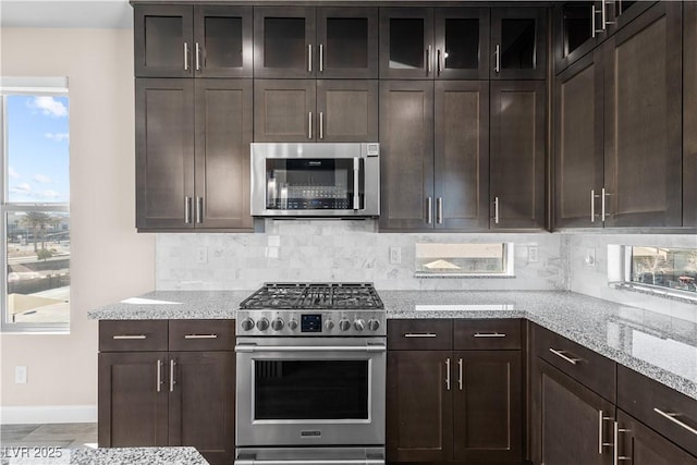 kitchen featuring stainless steel appliances, light stone countertops, tasteful backsplash, and dark brown cabinets